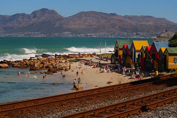 Muizenberg Beach in Cape Town with colourful bathing huts and surfers in False Bay