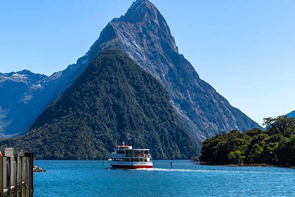 Small cruise boat travelling close to the cliffs of Milford Sound