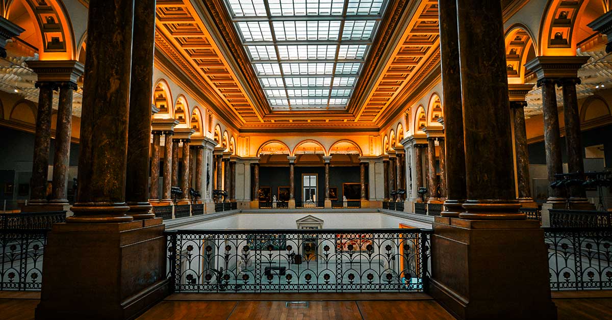 Interior of a grand New York museum gallery with visitors surrounded by works of art